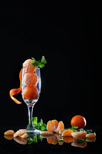 Kleine Mandarinen mit Minze in einem hohen Weinglas auf schwarzem Hintergrund. — Stockfoto