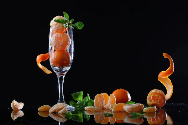 Small tangerines with mint in a tall wine glass on a black background. — Stock Photo, Image