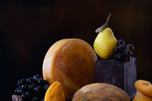 Stillleben von großen Stücken Hartkäse und Obst auf schwarzem Hintergrund. Stilllebenkonzept. — Stockfoto
