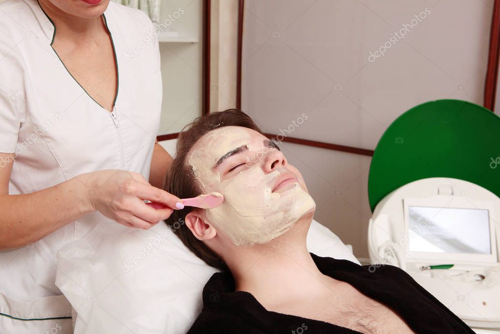 Cosmetic mask on the face of a young man. The beautician applies a nourishing mask.
