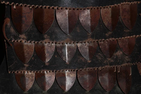 Protective metal plates on clothing. Macro-photo of the clothing of a warrior. Copy space. Brown metallic texture on black background.