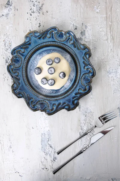 Pancake or dessert with vanilla sauce and blueberries on a blue ceramic plate. Fork and knife next to the plate.The view from the top. — Stock Photo, Image