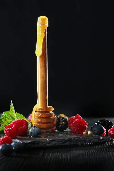 Stick untuk madu dengan buah beri pada latar belakang hitam. Madu mengalir ke bawah tongkat. Salin ruang . — Stok Foto