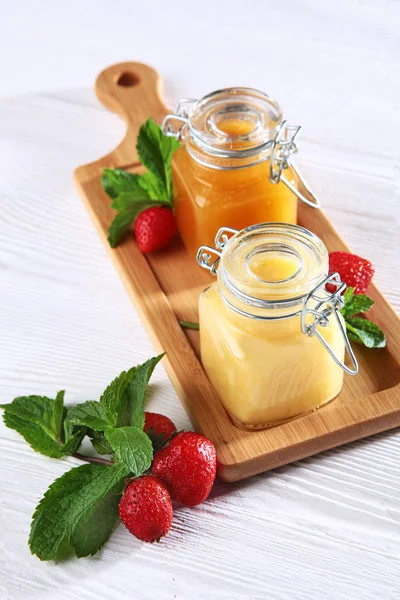 Dois jarros de mel em uma tábua de madeira com morangos em um fundo branco. Concepção de vida morta. Vista de cima . — Fotografia de Stock