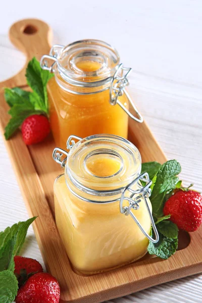 Honey in jars on a wooden board with strawberries on a white background. Still life concept. View from above. Macro photo. — Stock Photo, Image