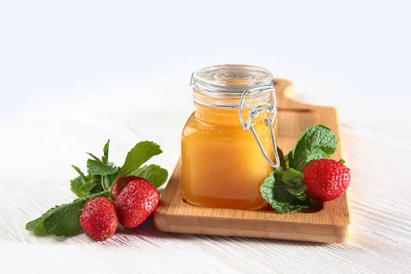 Jar of honey on a wooden board with strawberries on a white background. Still life concept. View from above. — Stock Photo, Image