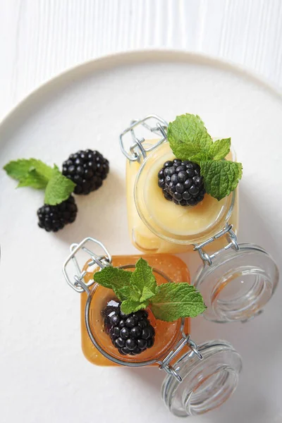 Two jars of honey and blackberries on a white plate. The view from the top. Photo on white background. Copy space. — Stock Photo, Image