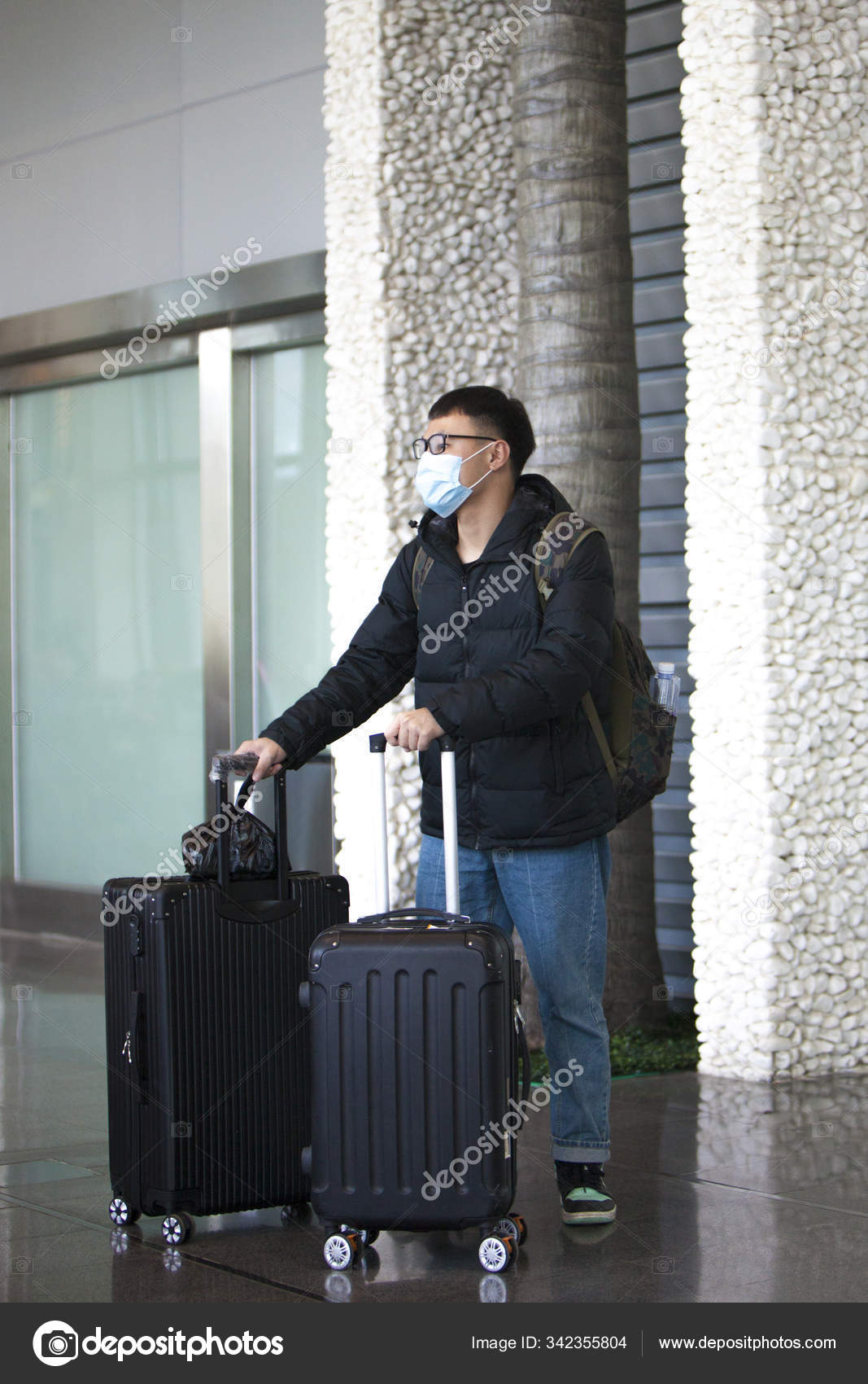 A Chinese man at the airport with suitcases and a medical mask on