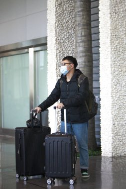 Havaalanında bavulları ve yüzünde sağlık maskesi olan bir Çinli. Çin 'de Coronavirus. 2020 'de küresel bir salgın tehdidi.