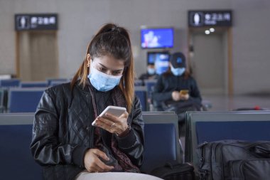 Kız havaalanında oturuyor ve Çin 'den ayrılıyor. Bir telefon tutuyorum. Yüzünde tıbbi maske var. 2020 'de Çin' de Coronavirus. Salgın tehdidi.