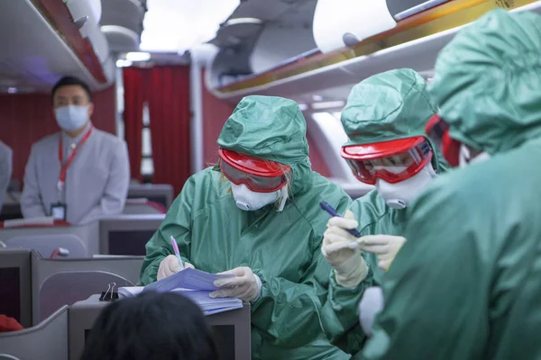 Drei Menschen in speziellen Schutzanzügen vor Viren und Bakterien nehmen an Bord eines aus China gekommenen Flugzeugs Tests vor. Unerkennbare Gesichter. Coronavirus 2019. Seuchengefahr. Unscharf . — Stockfoto