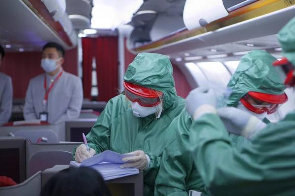 Virüs ve bakterilerden korunan özel giysiler içindeki tanınmayan kişiler yolcuları muayene ediyor ve Çin 'den gelen uçakta testler yapıyorlar. Coronavirus 2019. Salgın tehdidi var. Dışarı 