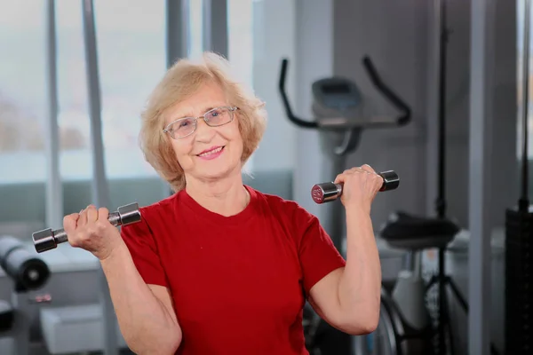 Una anciana sostiene pesas en sus manos. Concepto de retiro activo . —  Fotos de Stock