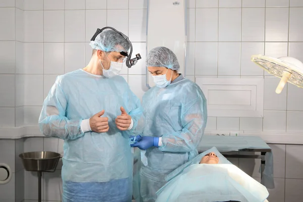 The nurse puts on a protective coat to the surgeon before the operation. A dentist surgeon is preparing for surgery. Photo in the operating room. — Stock fotografie