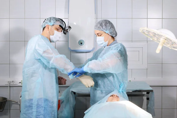 O asistentă medicală ajută la punerea mănușilor la un chirurg medic înainte de operație. Sănătate și frumusețe concept. Fotografie în sala de operație . — Fotografie, imagine de stoc