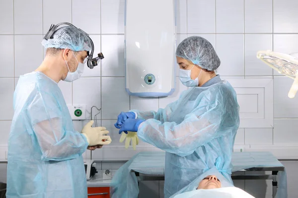 A nurse assistant helps put on gloves to a doctor surgeon before surgery. Health and beauty concept. Photo in the operating room. — Stock fotografie