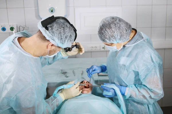 The dentist surgeon and assistant bent over the patient. Photo from above in the operating room. — Stock fotografie
