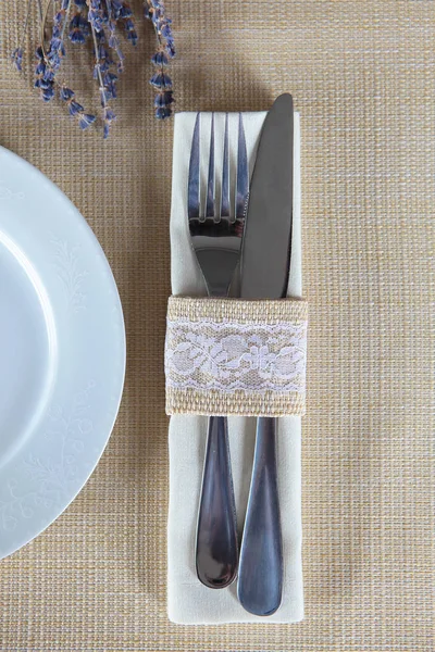 Table setting with a bouquet of lavender for the holiday. Beige color on tablecloths and napkins . The knife and fork are connected by a fabric ring with lace. Concept of restaurant and hotel business — Stock Photo, Image