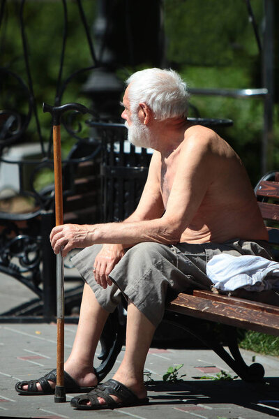An elderly, old man sits on a park bench. Concept of old age. Photo in the park.
