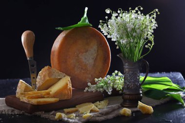 Bir peynir bıçağı ve bir buket sert peynir ve arka planda bir buket zambak. Süper manzara. Boşluğu kopyala.