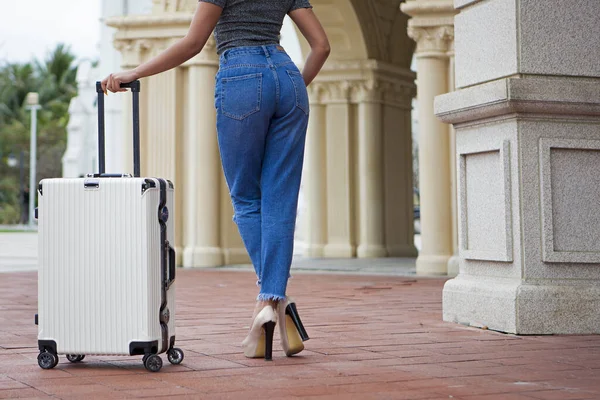 A girl stands with a suitcase on the street. Photo unrecognizable, rear view. The concept of travel and leisure. — Zdjęcie stockowe