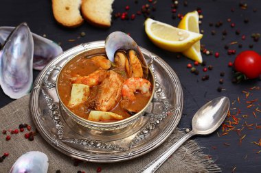 French seafood soup. Bouillabaisse ear of seafood. Vintage silver plated plate and spoon. Black background, top view. Free space for inscriptions. Still life concept.