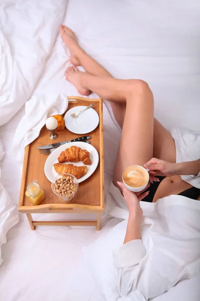 The girl is lying on the bed , and next to her is a tray with Breakfast. The view from the top. A photo without a face is unrecognizable. — Stockfoto