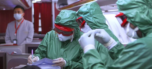 Three people in protective clothing from viruses and microbes work on Board the plane, taking tests from passengers. The threat of coronavirus 2019 China. Prevention of the epidemic. Unrecognizable