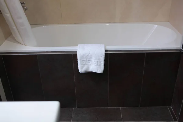A white foot towel hangs on the edge of the tub. Concept of hotel business and recreation. Comfort and cleanliness in the bathroom. Copy space.Top view