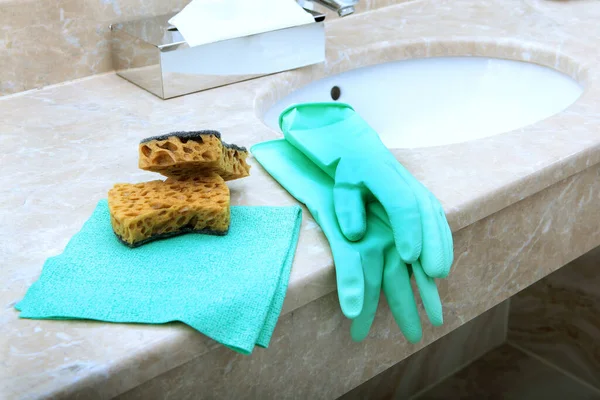 Green rubber or latex gloves and a cleaning sponge lie on the marble sink in the bathroom. The view from the top. Items of sanitary hygiene and disinfection. Copy space.