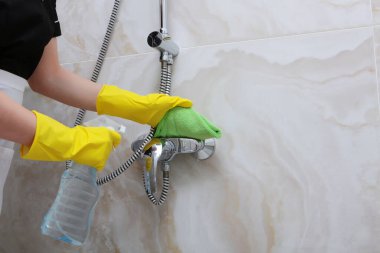 Sarı lastik eldivenli eller duş kabinindeki musluğu yıkıyor. Tanımlanamayan fotoğraf. Otelde ya da evde temizlik..