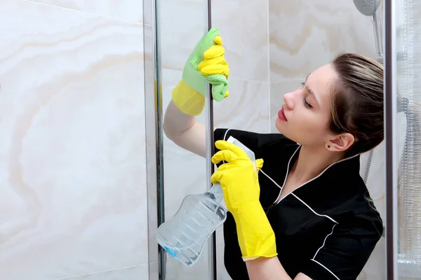 Una joven en uniforme y guantes de goma lava el puesto de ducha. Cerca - arriba de las manos. Servicio de limpieza en el hotel o en casa . — Foto de Stock