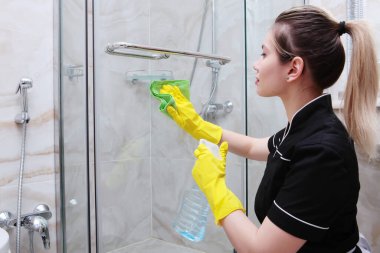 Duş kapısı temizlikçi kıyafetli genç bir kız tarafından açılabilir. Yüzü bulanık. Temizlik ve hijyen kavramı.