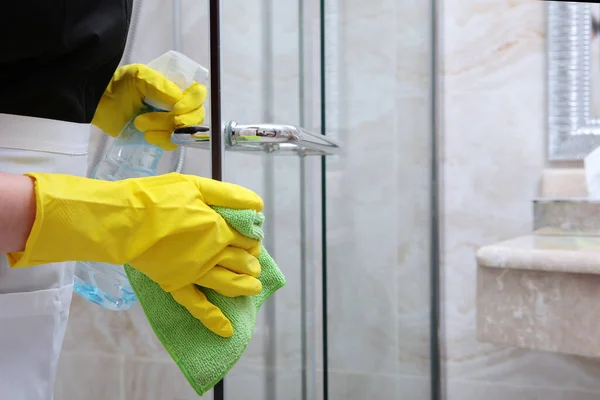 Una mujer del servicio de limpieza lava las puertas transparentes del puesto de ducha. Foto irreconocible. El concepto de limpieza e higiene . — Foto de Stock