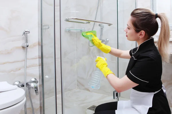 Puertas de ducha transparentes pueden ser abiertas por una niña en un traje de servicio de limpieza. La cara está borrosa. El concepto de limpieza e higiene . — Foto de Stock