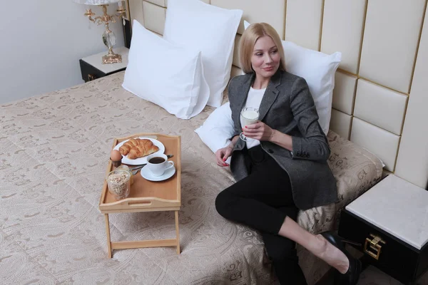 A young businesswoman is having Breakfast in bed in business clothes. The model doesnt look at the camera. Copy of the space.