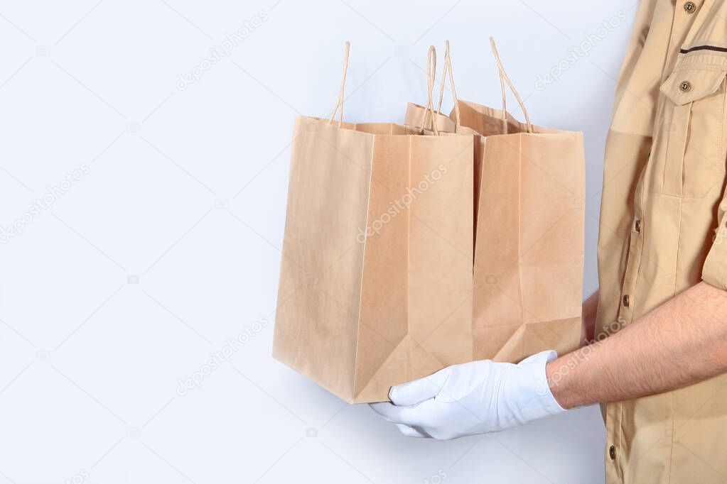 Mens hands in white gloves hold two paper bags with purchases. The concept of service delivery. Unrecognizable photo. Copy of the space.