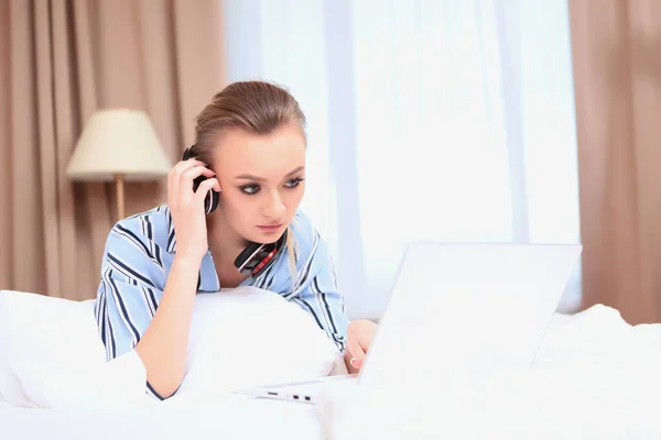 Egy fiatal lány fekszik az ágyon, és a laptop képernyőjét nézi. A távoktatás vagy az otthoni munkavégzés fogalma. Egy másolat erről a helyről.. — Stock Fotó