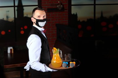 Yüzünde koruyucu, neşeli bir maske olan genç bir garson. Elinde mikrofon ve bir sürahi limonata olan bir tepsi. Salgın tehdidi. COVID-19