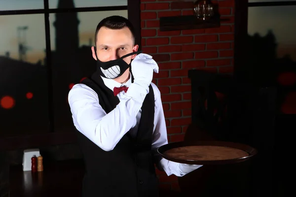 Genç bir garson yüzünden komik bir maske çıkarıyor. Virüsün yayılmasını engelliyor. Salgının sonu geldi. Koronavirüs tehdidi. Mekanın bir kopyası. Tamam. 19.