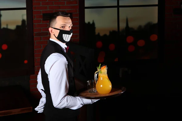 Un camarero con una divertida mascarilla lleva una bandeja de limonada en la mano. Servicio de atención al cliente restaurante. La amenaza de una pandemia COVID-19 — Foto de Stock