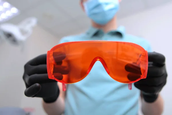Orange skyddsglasögon i händerna på en tandläkare. Oigenkännlig bild. — Stockfoto