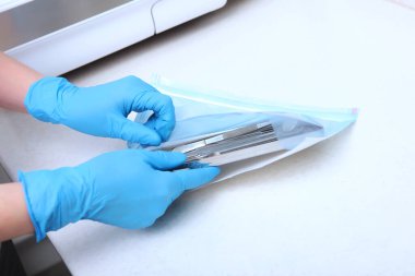 Mavi eldivenli bir tıp çalışanının elleri sterilizasyon için diş aletleri taşır. Tanımlanamayan fotoğraf. Sadece el..