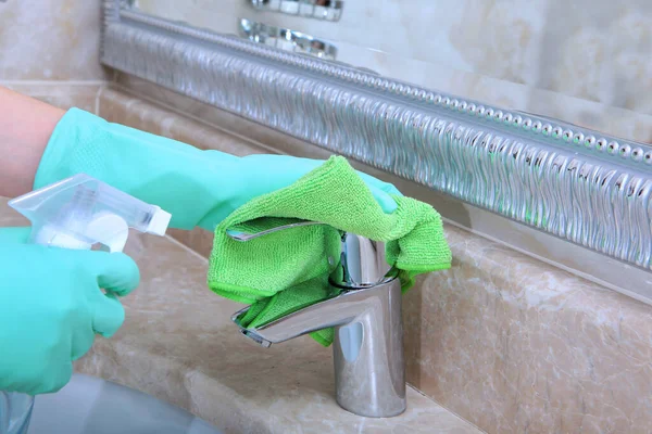 Hands in green rubber gloves clean the faucet in the bathroom. Unrecognizable photo. The concept of cleanliness and hygiene in the hotel.