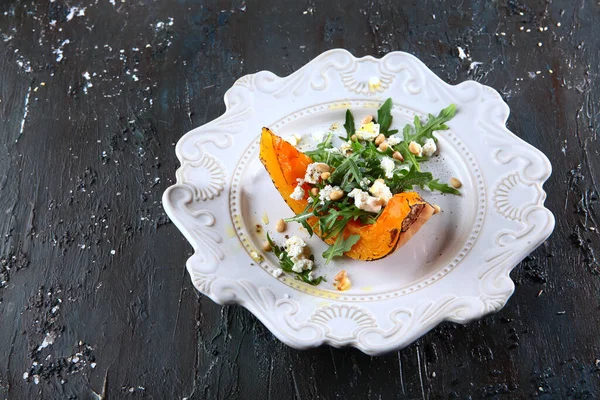 Beyaz tabakta roka ve çam fıstığı ile fırında kabak peyniriyle. Karanlık desenli bir arka planda fotoğraf. Üst Manzara. Boşluğu kopyala.