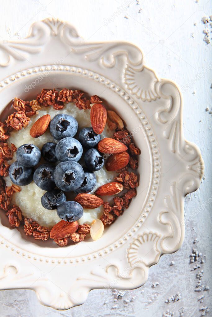 Rice porridge with blueberries or blueberries and almonds in a white plate.Macro photo of the dish on a light textured background. Copy space. Top view.