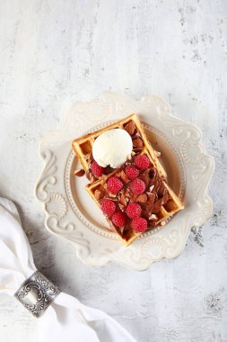 Çikolatalı waffle ve ahududu. Gofretlerin üzerinde bir top dondurma var. Işık arkaplanındaki fotoğraf. Beyaz tabakta bir tabak. Üst Manzara. Boşluğu kopyala.