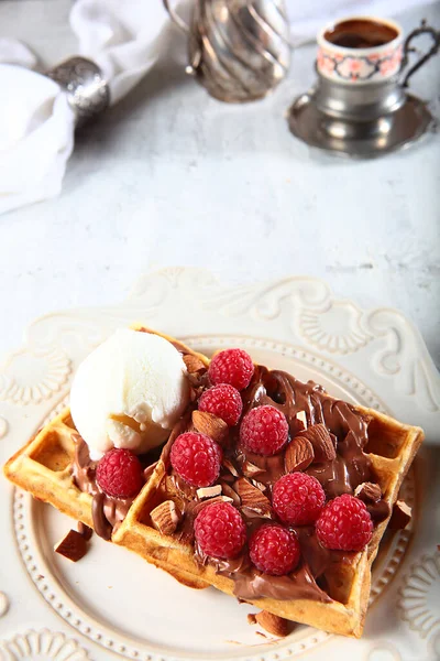 Çikolatalı waffle ve ahududu. Gofretlerin üstünde bir top dondurma var. Arka planda antika sofra takımı. Beyaz tabakta bir tabak. Üst Manzara. Boşluğu kopyala.