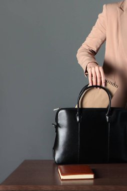Bir kadının eli iş defterini çantasına koyar. Tanımlanamayan fotoğraf. Gri nötr arka plan. Boşluğu kopyala.