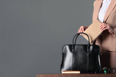 Bir kadının eli iş defterini çantasına koyar. Tanımlanamayan bir fotoğraf. Tarafsız gri arkaplanlı yatay bir fotoğraf. Boşluğu kopyala.